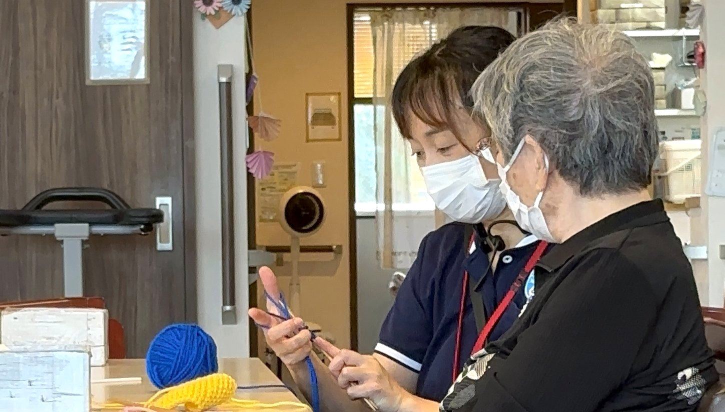 毛糸の編み方を一緒に確かめる職員とご利用者